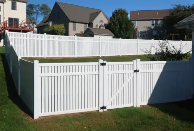 White vinyl fence with a gate enclosing a green backyard in a suburban residential area.
