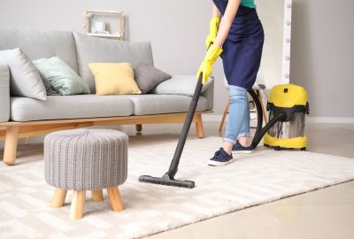 Person wearing yellow gloves and a blue apron vacuuming a rug in a living room.