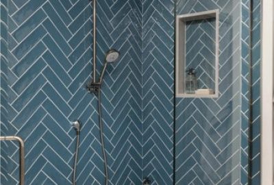 Shower stall with blue herringbone tiled walls, a handheld showerhead, and a built-in wall niche.