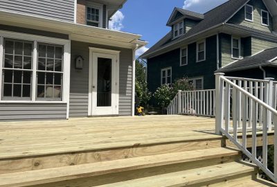 New unfinished wooden deck with white railings and stairs attached to a gray house.