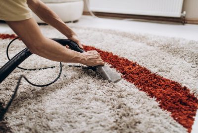 Hands using a carpet cleaning tool on a white shaggy rug with a red stripe.