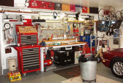 A cluttered workshop with red tool chests, a workbench with tools on a pegboard, and bicycles hanging on the wall.