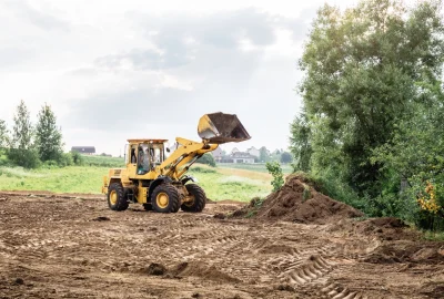 Yellow front-end loader with raised bucket in a dirt field next to a pile of soil.