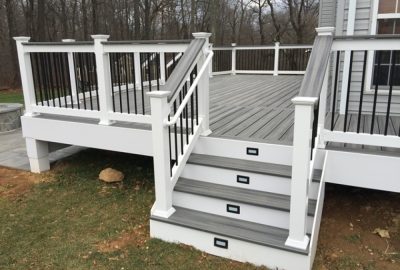Raised backyard deck with gray composite decking, white railings, black balusters, and stairs with integrated lighting.