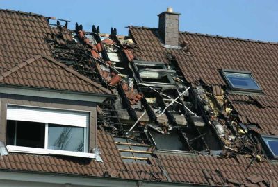 Fire-damaged brown tiled roof with a large hole exposing charred wooden support beams.