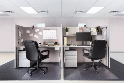 Two side-by-side modern office cubicles with black leather chairs, white desks, and grey partitions.