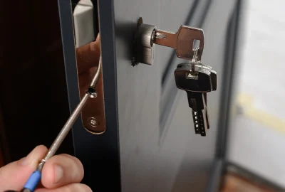 A person manipulating a door lock's internal mechanism with a thin tool while a key is inserted in the lock.