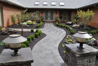 A paved stone walkway leads through a landscaped yard to the front entrance of a brick house with two matching lanterns.