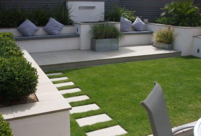 Modern landscaped garden with a manicured lawn, stone stepping stones, and a patio with built-in seating.