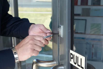 Person using lock-picking tools to open a glass door lock.