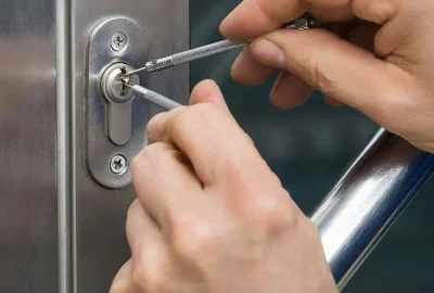 Hands using lock-picking tools to open a silver door lock.