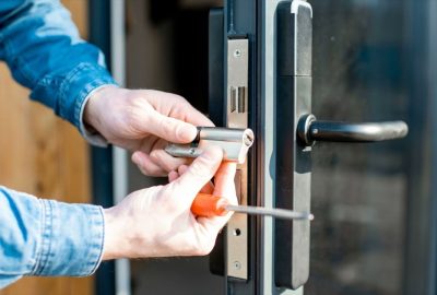 Hands using a screwdriver to install a silver lock cylinder into a black door frame.