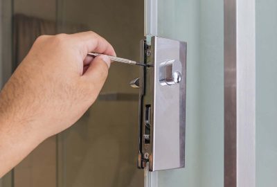 Hand using a precision tool to manipulate a silver lock mechanism on a glass door.