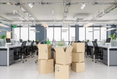 Stack of open and closed cardboard boxes in the center of an empty, modern office space.