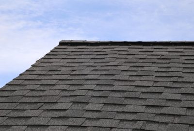 Grey asphalt shingle roof ridge against a light blue sky.