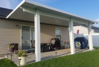 White patio cover installed over a concrete backyard patio with outdoor furniture and a covered grill.
