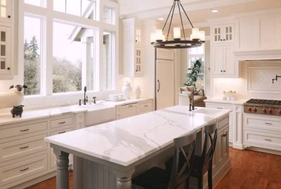 Bright farmhouse kitchen with white cabinetry, marble countertops, a large central island, and expansive windows.