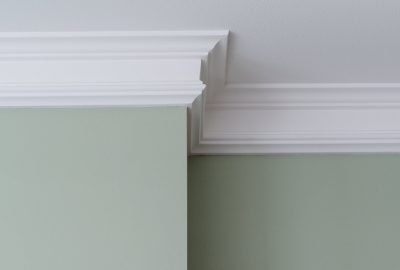 White decorative crown molding installed at the corner of a sage green wall and a white ceiling.