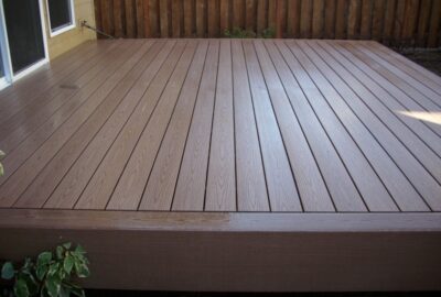 Brown composite deck with wood-grain planks and a wooden privacy fence in the background.