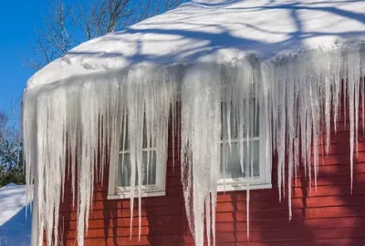Large icicles hanging from the roof of a red house covered in snow.