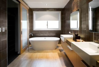 Modern bathroom with a white freestanding bathtub, double sinks on a wooden vanity, and dark grey tiled walls.