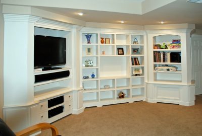 Built-in white media center and shelving unit with a television, various decorative items, and books.