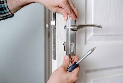 Person using a screwdriver to install a silver door handle on a white door.