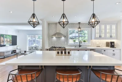 Modern open-concept kitchen with a white island, bar stools, and geometric pendant lights overlooking a living room.