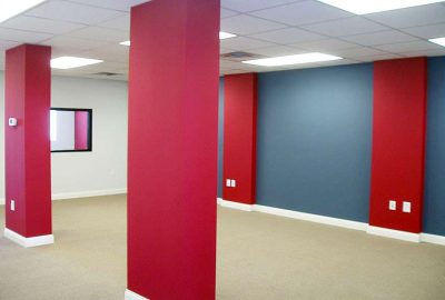 Interior office space featuring red accent columns, blue walls, beige carpeting, and a drop ceiling with recessed lighting.