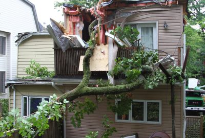Large fallen tree crushing the roof and second-story balcony of a residential home.