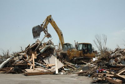Yellow excavators clearing a massive pile of wooden debris and rubble at a disaster site.