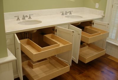 White double sink bathroom vanity with open cabinets revealing custom U-shaped wooden pull-out drawers.