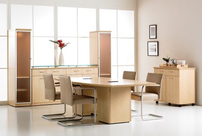 Modern conference room with light wood table, tan leather chairs, and matching storage cabinets in a bright space.