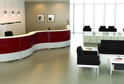 Modern office reception area with a curved red and white desk and black lounge seating.