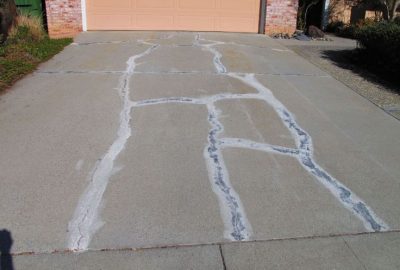 Concrete driveway with large, irregular cracks filled with white sealant leading to a garage.