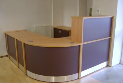 L-shaped reception desk with light wood trim and dark purple panels in a room with light wood flooring.