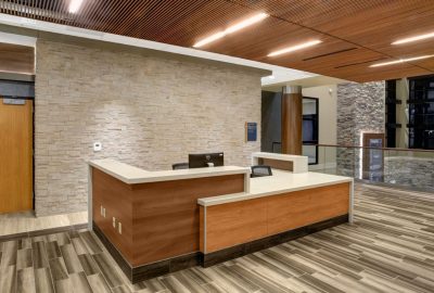 Modern office reception desk with wood paneling, white countertops, and a light stone feature wall.