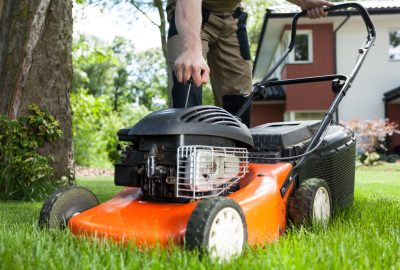 Person pulling the starter cord of an orange lawnmower in a green yard.