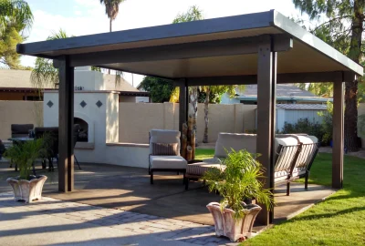 Outdoor patio with a dark wooden pergola covering lounge furniture, a paved area, and a manicured lawn.