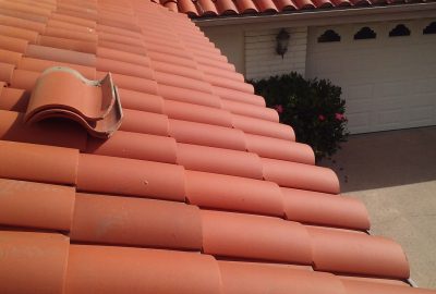 Close-up of a red terracotta tile roof with one tile broken and displaced from the ridge.