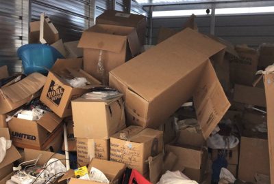 Cluttered storage unit filled with disorganized cardboard boxes and a blue plastic bin.