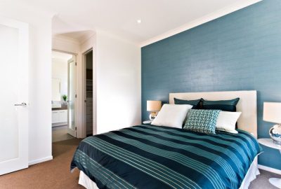 Modern bedroom with a teal accent wall, striped blue bedding, white pillows, and white nightstands with lamps.