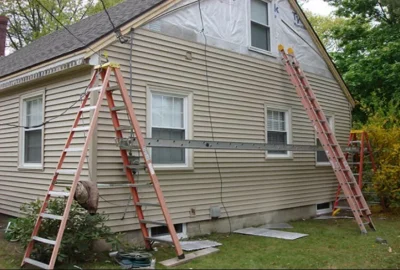 Two orange ladders and a metal scaffolding platform set up against a tan house with light beige siding.