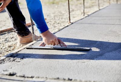A mason using a concrete trowel to finish a newly poured concrete slab with shallow depth of field