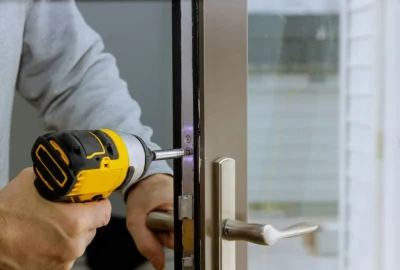 Person using a yellow cordless drill to secure a screw in a glass door hinge.