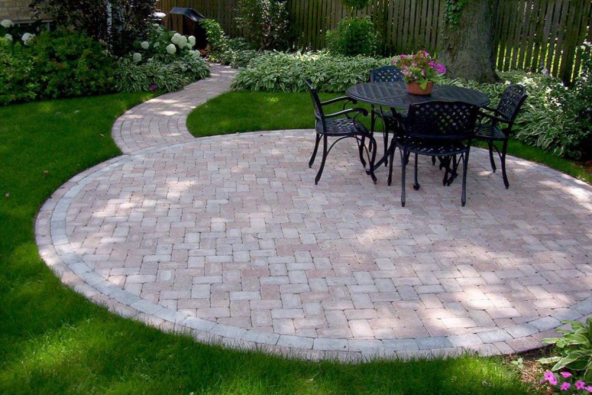 Circular stone patio with a black wrought-iron dining set and a winding stone path in a lush green garden.