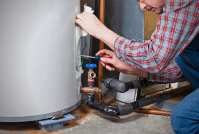 Technician in a plaid shirt using a screwdriver to repair a residential water heater.
