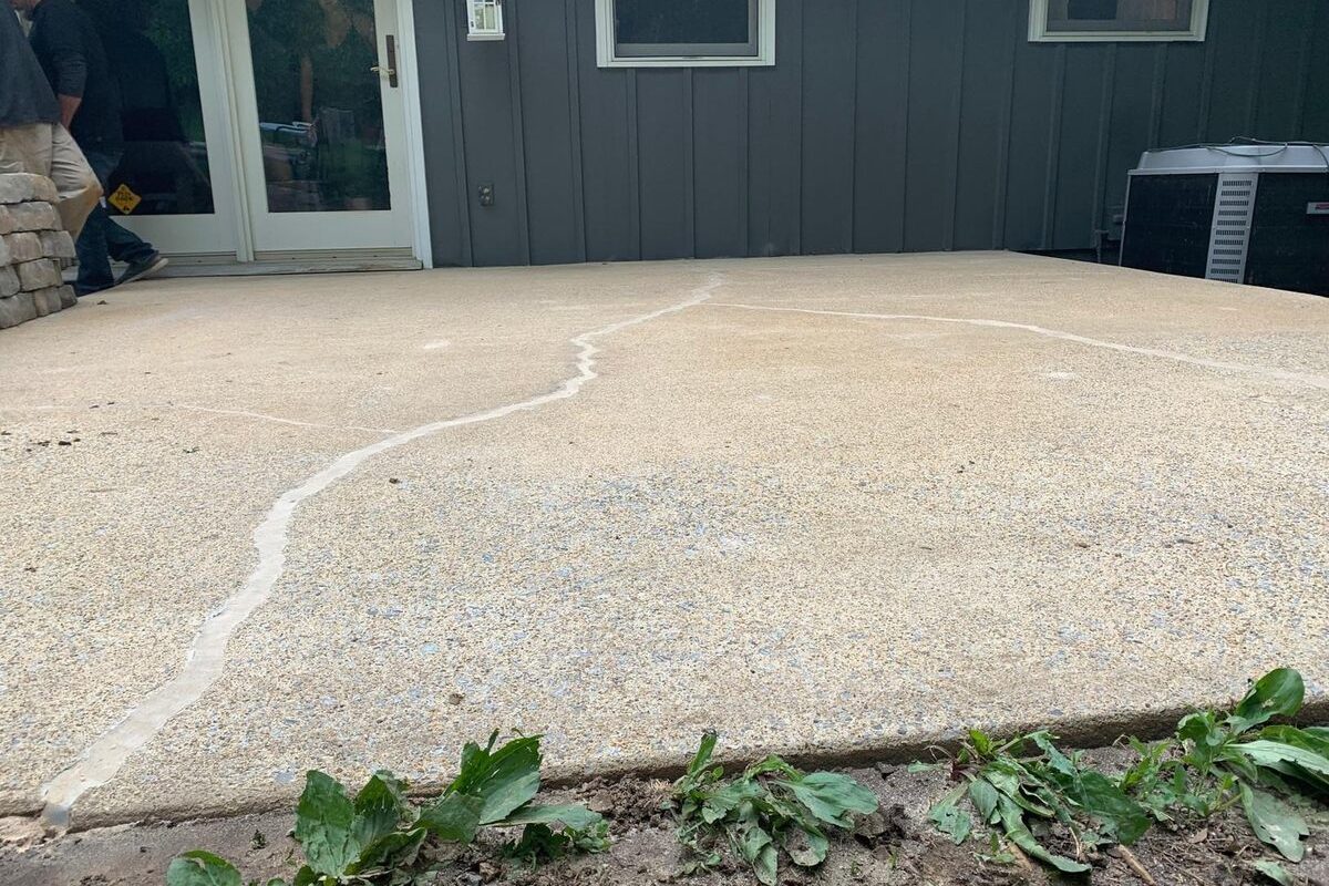 Concrete patio with winding cracks filled with white sealant next to a dark gray house.