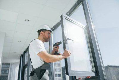 Construction worker in a hard hat using a power drill on a window frame.