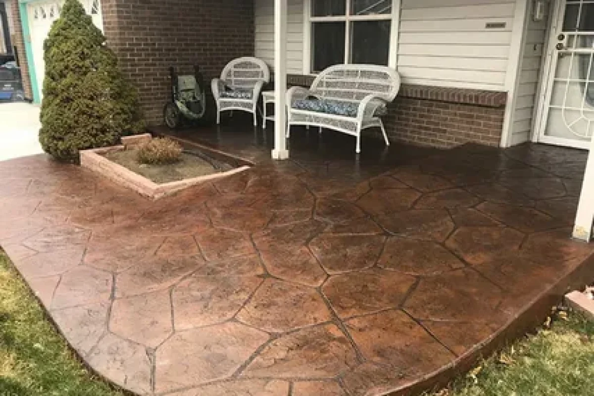Brown stamped concrete patio with a flagstone pattern, white wicker furniture, and a brick house exterior.